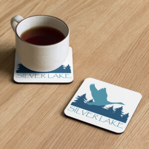 cork back coaster front with a stylized teal blue logo for 'History of Silver Lake' book: A single goose flying over Silver Lake with trees in the background.