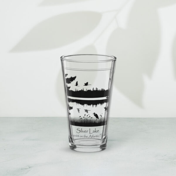 shaker pint glass 16 oz 16 oz front with an image of Silver Lake featuring a blue heron in the foreground and Canada Geese in flight overhead, highlighting Silver Lake as a waypoint on the American Atlantic Flyway from historyofsilverlake.com website.