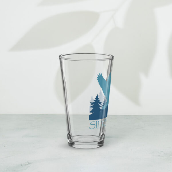 shaker pint glass 16 oz 16 oz right with a stylized teal blue logo for 'History of Silver Lake' book: A single goose flying over Silver Lake with trees in the background.