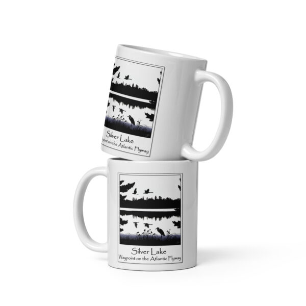 white glossy mug white 11 oz front view with an image of Silver Lake featuring a blue heron in the foreground and Canada Geese in flight overhead, highlighting Silver Lake as a waypoint on the American Atlantic Flyway from the book "The History of Silver Lake as Told Through Its Deeds".